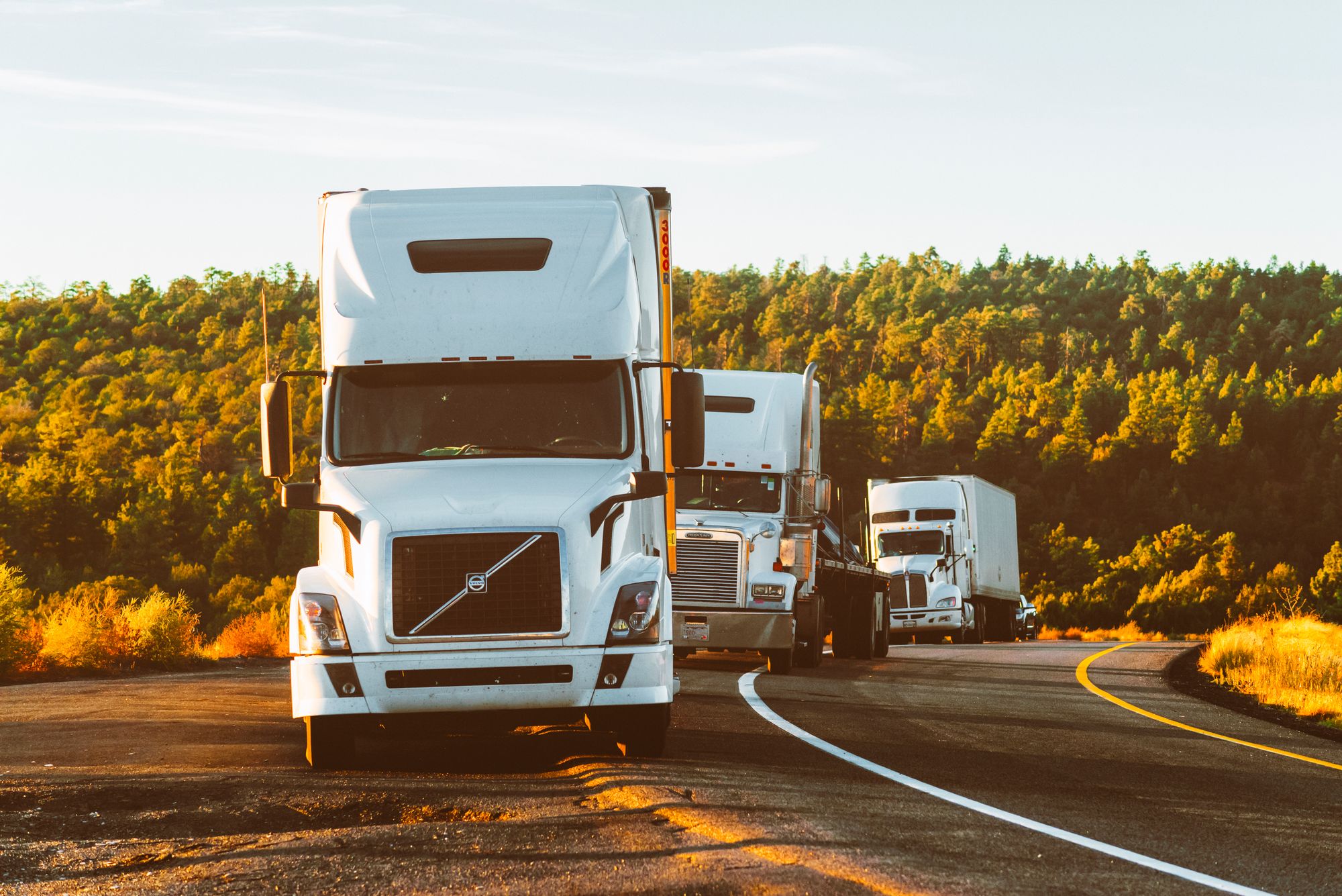 White tractor-trailers travelling on a North American highway; illustrative stock photograph.